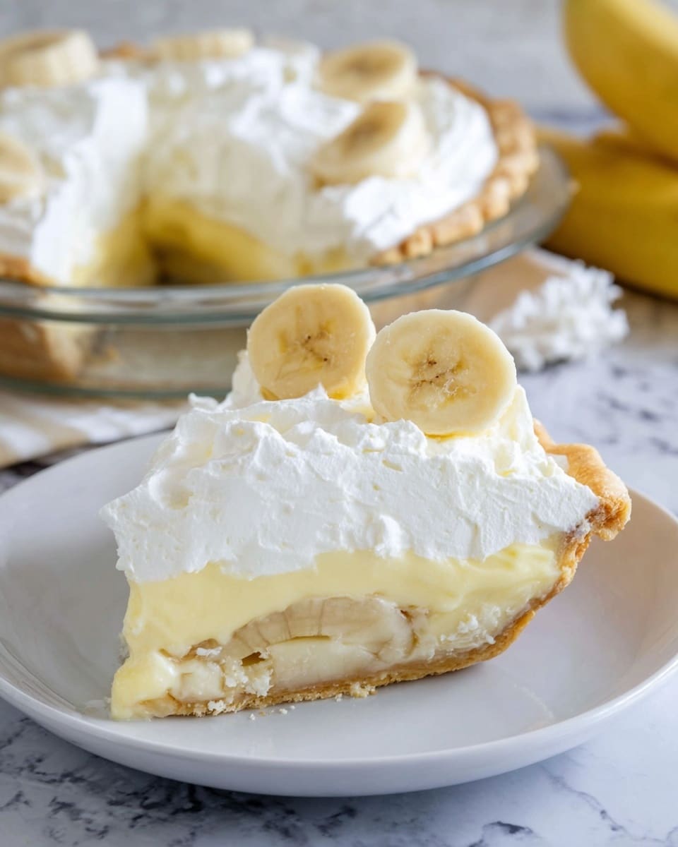 A slice of banana cream pie sits on a white plate with three visible layers: the bottom layer is a light golden, flaky pie crust; above it is a thick pale yellow banana cream filling with banana slices embedded within; the top layer is a fluffy, smooth white whipped cream covering the entire slice, garnished with two fresh banana slices standing upright near the back edge. The background shows the rest of the pie in a clear glass pie dish, set on a white marbled surface. photo taken with an iphone --ar 4:5 --v 7
