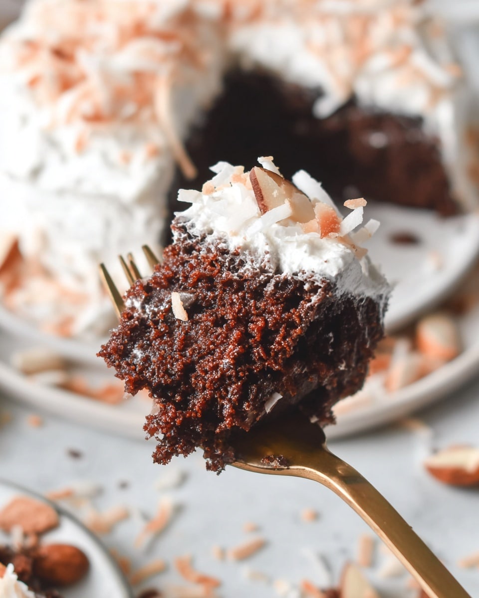 A close-up view of a moist dark brown chocolate cake piece with a crumbly texture on a golden fork, topped with white shredded coconut flakes and white frosting. In the background, part of the remaining cake is visible with thick white frosting and coconut flakes on top, sitting on a white plate on a white marbled surface scattered with more coconut flakes and nut slices. photo taken with an iphone --ar 4:5 --v 7
