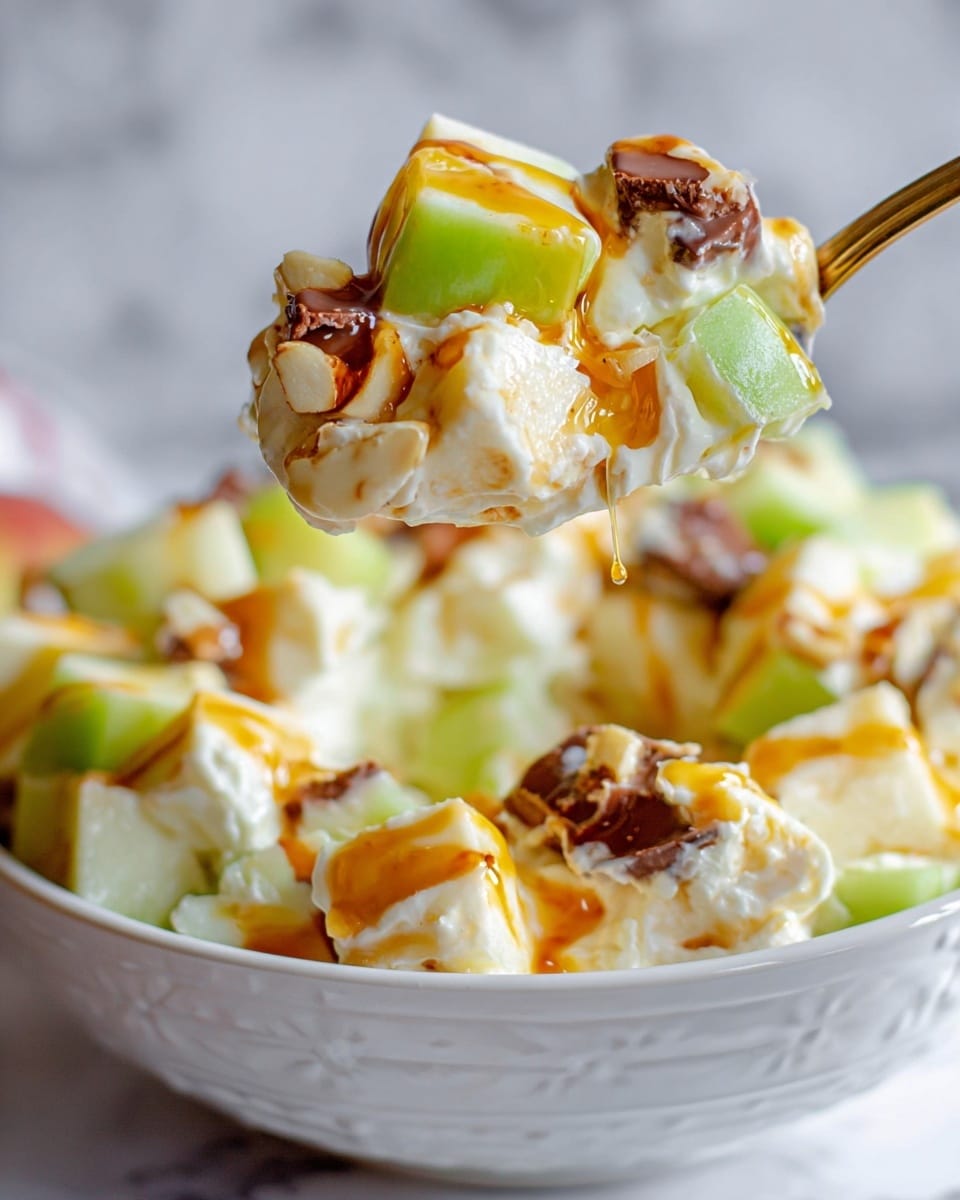 This image shows a close-up of a spoonful of creamy fruit salad lifted above a white bowl on a white marbled surface. The spoon holds several layers: glossy green apple cubes, soft white cream, light yellow chunks likely pineapple, and small brown pieces that look like chocolate or nuts. There is a drizzle of orange syrup or sauce on top adding shine. The bowl below is filled with the same mixed salad layers with a creamy texture and scattered colorful chunks. photo taken with an iphone --ar 4:5 --v 7