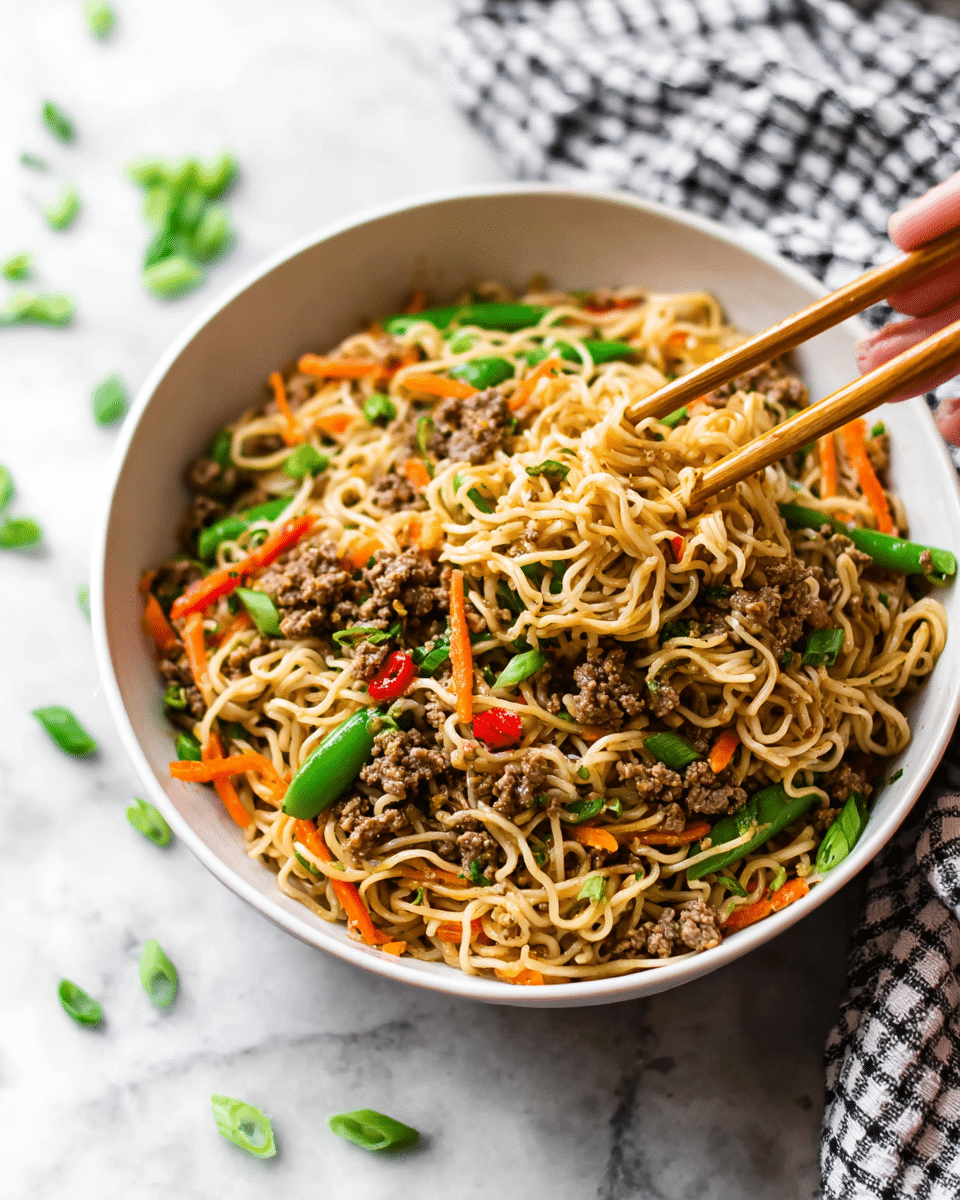 A white bowl filled with a mixed noodle dish showing soft, light brown noodles tangled with cooked ground meat, bright green snap peas, orange carrot strips, and small red chili pieces, all topped with chopped green onion bits. Two wooden chopsticks are stuck into the noodles at the back of the bowl, with a small part of a woman's hand holding one of them. The bowl sits on a white marbled surface with some scattered green onion slices and carrot pieces around it. A checkered cloth is visible in the blurred background. photo taken with an iphone --ar 4:5 --v 7