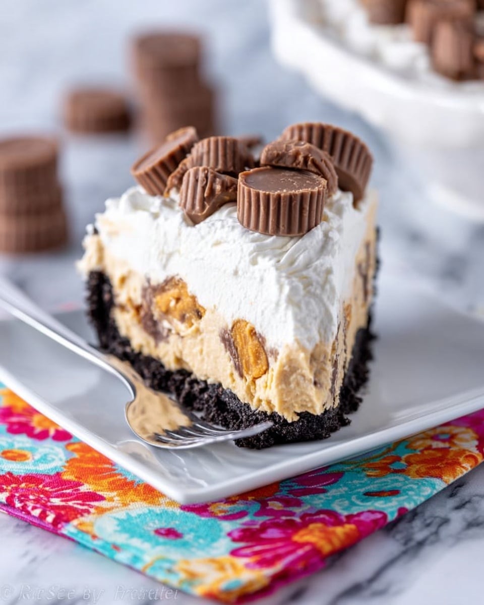 A slice of layered dessert sits on a white square plate placed over a colorful floral napkin on a white marbled surface. The bottom layer is a dark chocolate crumb crust, topped by a thick creamy peanut butter layer with pieces of peanut butter cups mixed in. Above that, there is a layer of fluffy white whipped cream, crowned with several mini peanut butter cups arranged on top. A silver fork rests beside the dessert on the plate. The background is softly blurred with a hint of more dessert pieces. Photo taken with an iphone --ar 4:5 --v 7