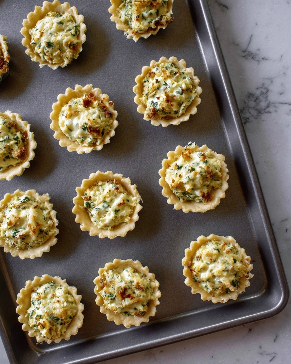 This image shows a baking tray holding eleven mini tart cups arranged loosely in rows. Each tart cup is filled with a creamy mixture that includes small bits of green herbs and browned onion pieces, giving a textured look with hints of yellow, light green, and brown colors. The tart shells have crimped edges that are golden brown, adding a crispy contrast to the creamy filling. The tray sits on a surface with a white marbled texture, providing a clean and simple background. The photo taken with an iphone --ar 4:5 --v 7