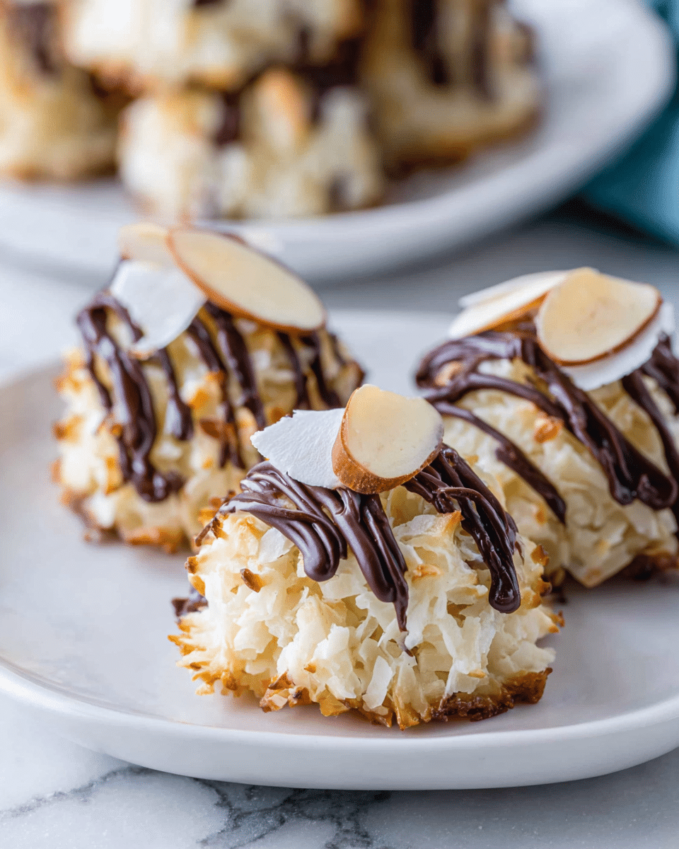 Three small, round coconut macaroons sit close together on a white plate. Each macaroon has a rough, textured outer layer of shredded coconut that is lightly toasted with small golden-brown spots. Dark chocolate is drizzled on top of each macaroon in thin, uneven lines that cover the upper half. On top of the chocolate drizzle, thin slices of almond with a light tan edge are placed as a final garnish. The plate rests on a white marbled surface with a blurred stack of more macaroons seen in the background. photo taken with an iphone --ar 4:5 --v 7