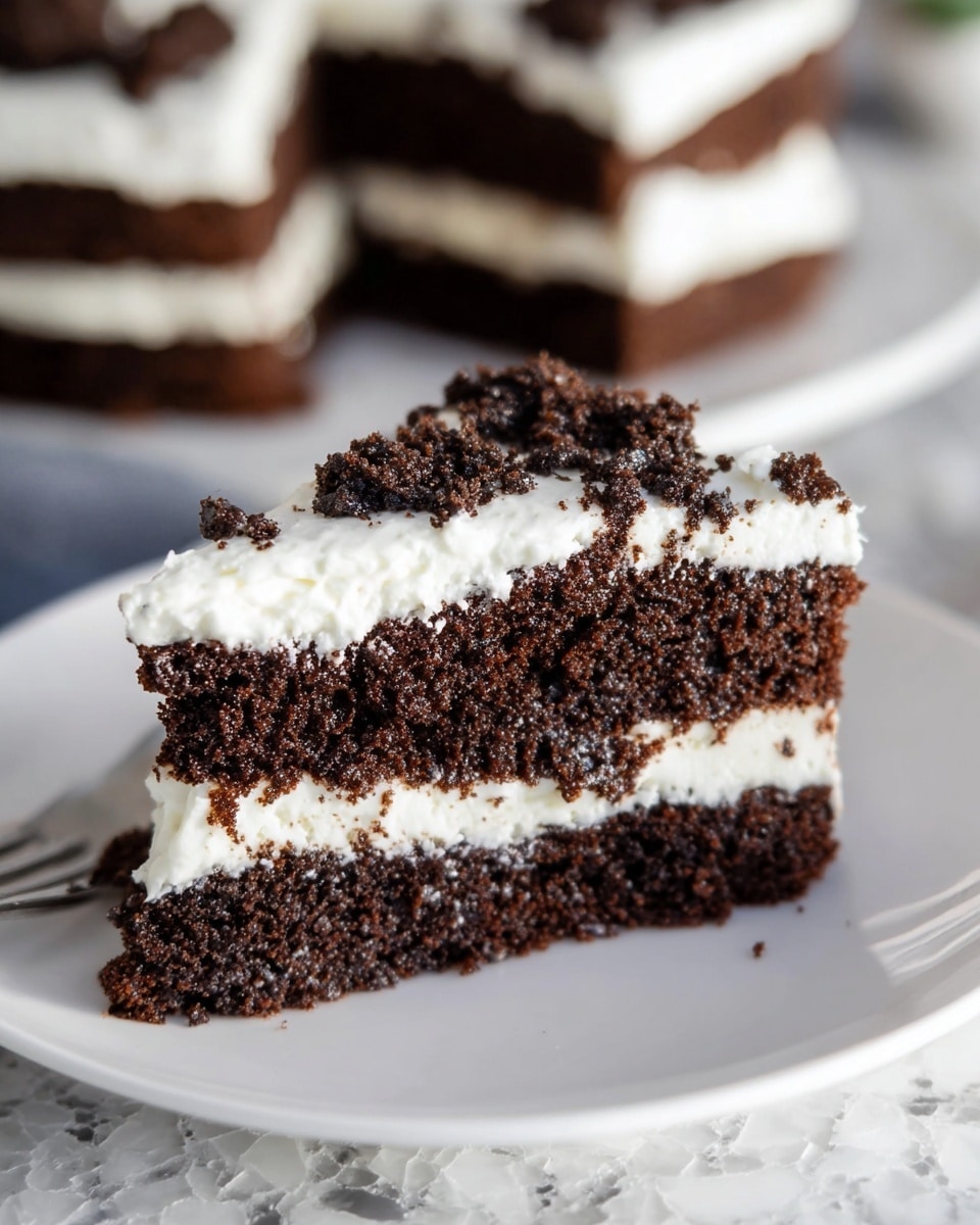 A close-up showing a layered dessert with a thick bottom layer of dark brown, crumbly chocolate cake topped with a thick layer of smooth, white whipped cream spread across the entire surface, dotted generously with small, loose chunks of chocolate cake crumbs scattered unevenly on top. The dessert sits on a white plate, placed on a bright, colorful patterned cloth on a white marbled surface. The texture contrasts between the creamy, soft whipped topping and the moist, crumbly chocolate pieces are clear. photo taken with an iphone --ar 4:5 --v 7