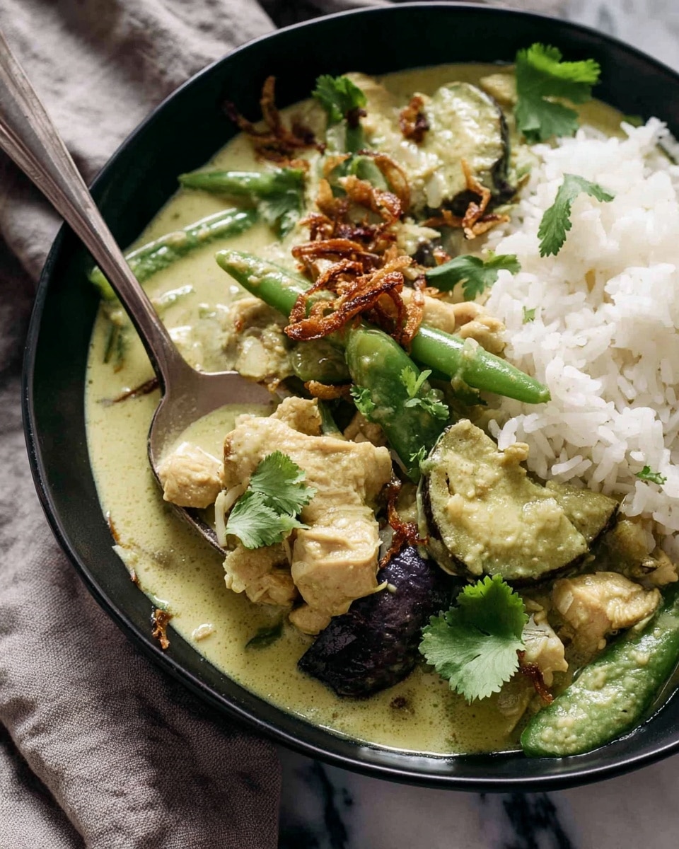 The image shows a close-up of a black bowl filled with a creamy green curry dish served alongside white rice. The curry has several layers: sliced green vegetables, pieces of chicken, and some dark purple vegetable slices, all coated in a thick, light green sauce. The dish is topped with crispy fried shallots and garnished with fresh cilantro leaves. A silver spoon rests in the bowl, scooping up some of the curry and rice. The background features a white marbled texture with a soft gray cloth partially visible. Photo taken with an iphone --ar 4:5 --v 7