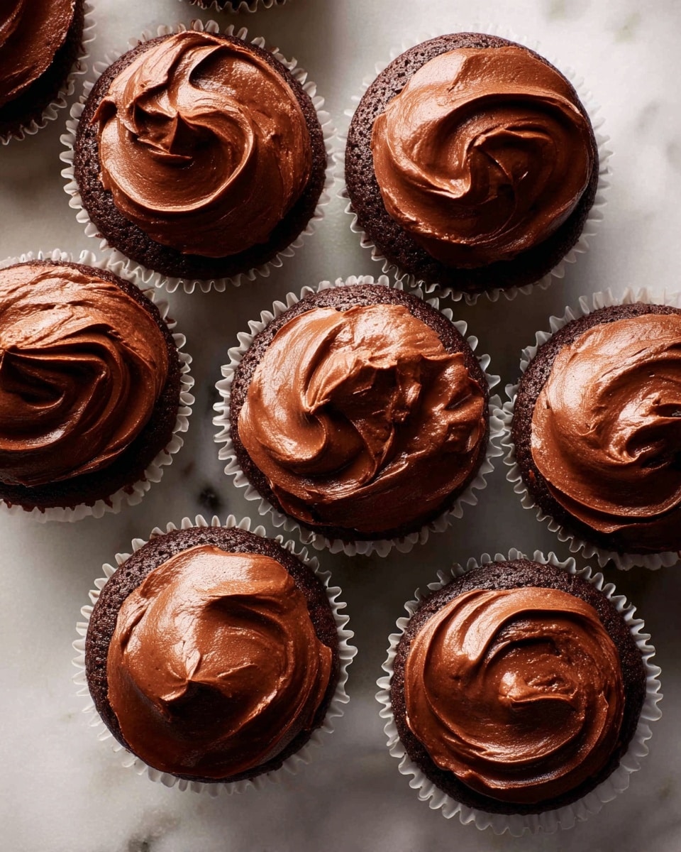 This image shows a group of nine chocolate cupcakes arranged closely together on a white marbled surface. Each cupcake has one layer of dark brown cake at the bottom, wrapped in white paper liners with slightly ruffled edges. On the top of each cupcake, there is a thick, smooth layer of shiny chocolate frosting with swirl patterns, creating a rich texture. The frosting varies a bit in shape on each cupcake but all have a glossy, creamy appearance. The overall look is neat and inviting, with a warm brown color dominating the scene. photo taken with an iphone --ar 4:5 --v 7