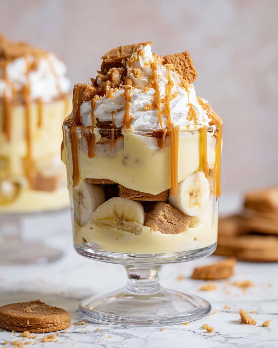 A clear glass dessert cup holds a layered banana pudding parfait on a white marbled surface. The bottom layer consists of light brown cookies, slightly visible through the glass along with banana slices pressed against the sides. Above this is a thick, smooth pale yellow pudding layer with more cookies and banana slices embedded within. A generous layer of whipped cream tops the parfait, drizzled with a caramel or peanut butter sauce that drips down the sides. Crumbled cookie pieces are sprinkled on top, adding texture. The background is softly blurred with a similar parfait in the distance, maintaining focus on the front dessert. Photo taken with an iphone --ar 4:5 --v 7
