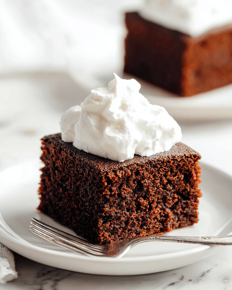 A close-up of a single square piece of chocolate cake on a white plate, showing one thick layer of moist, dark brown cake with a soft, crumbly texture. It is topped with a generous dollop of smooth, fluffy white whipped cream that sits slightly uneven on the cake. A silver fork rests on the plate beside the cake. In the background, there is another square piece of chocolate cake on a similar white plate, slightly blurred. The setting is on a white marbled surface. photo taken with an iphone --ar 4:5 --v 7