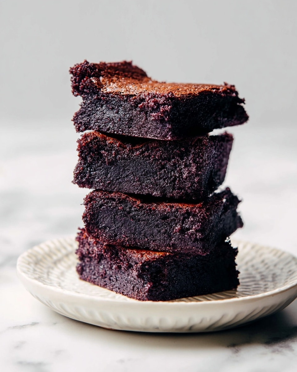 A stack of four dark chocolate brownies is placed on a white plate with a textured edge, sitting on a white marbled surface. Each brownie layer is thick, rich, and moist with a dense, slightly crumbly texture. The top brownie has a rough cracked surface, showing a soft interior, while the layers below are neatly stacked but slightly uneven in placement. The overall color is deep brown with hints of darker crust on the edges, emphasizing the fudgy nature of the brownies. Photo taken with an iphone --ar 4:5 --v 7