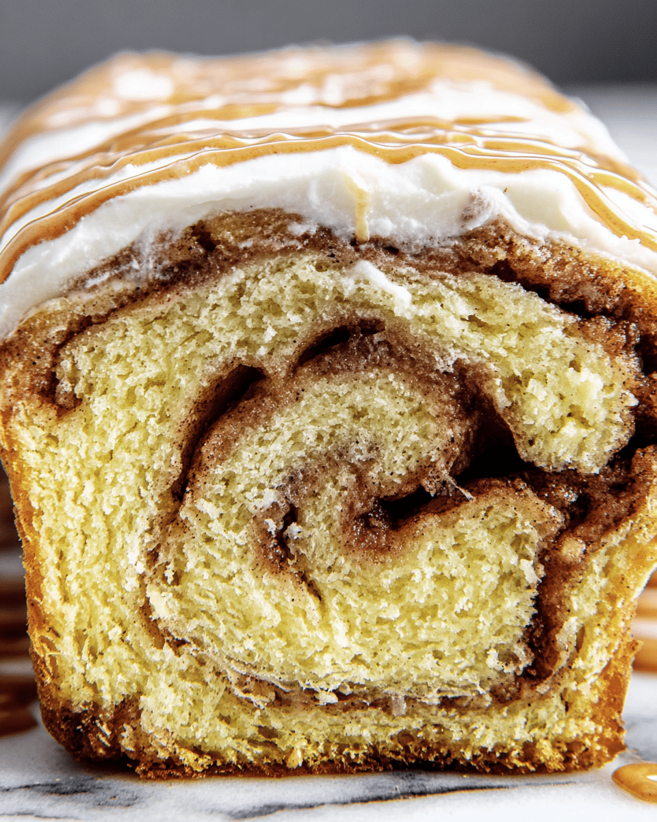 The image shows a close-up of a slice of cinnamon roll bread with three visible layers: a thick, light yellow dough base with a soft and moist texture, a dark brown swirled cinnamon sugar filling in the middle creating a spiral pattern, and a top layer covered in white cream cheese frosting with a smooth and slightly glossy texture. Additional thin ribbons of brown cinnamon glaze are drizzled on top of the frosting. The bread slice is placed on a white marbled surface. photo taken with an iphone --ar 4:5 --v 7