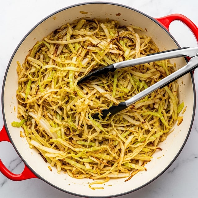 This is a close-up image of cooked shredded cabbage in a white pot with red rims and handles. The cabbage is light yellow and pale green with some brown crispy edges spread evenly in the pot, showing a mix of soft, wilted, and slightly crunchy textures. There are metal tongs with black tips resting on top, partially inserted into the cabbage, adding contrast to the yellow and green colors of the cabbage. The background is a white marbled texture. photo taken with an iphone --ar 4:5 --v 7