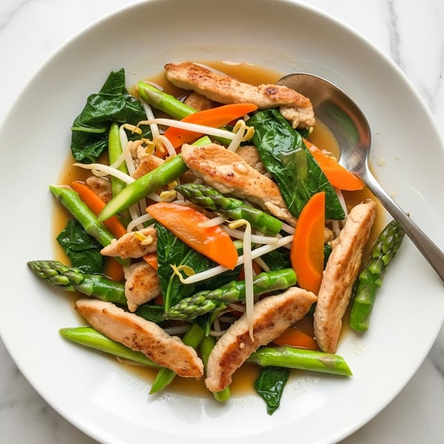 A white plate holds a dish with several layers: at the bottom are thin, light brown cooked chicken pieces with a slightly seared texture, scattered among bright green stalks of asparagus and dark green leafy vegetables. On top of these are thin, orange carrot slices and some white bean sprouts mixed throughout. The entire dish is covered with a shiny, light brown sauce that gives a glossy look to all ingredients. A silver spoon rests on the right side of the plate, partly inserted into the food. The plate sits on a white marbled surface. photo taken with an iphone --ar 4:5 --v 7