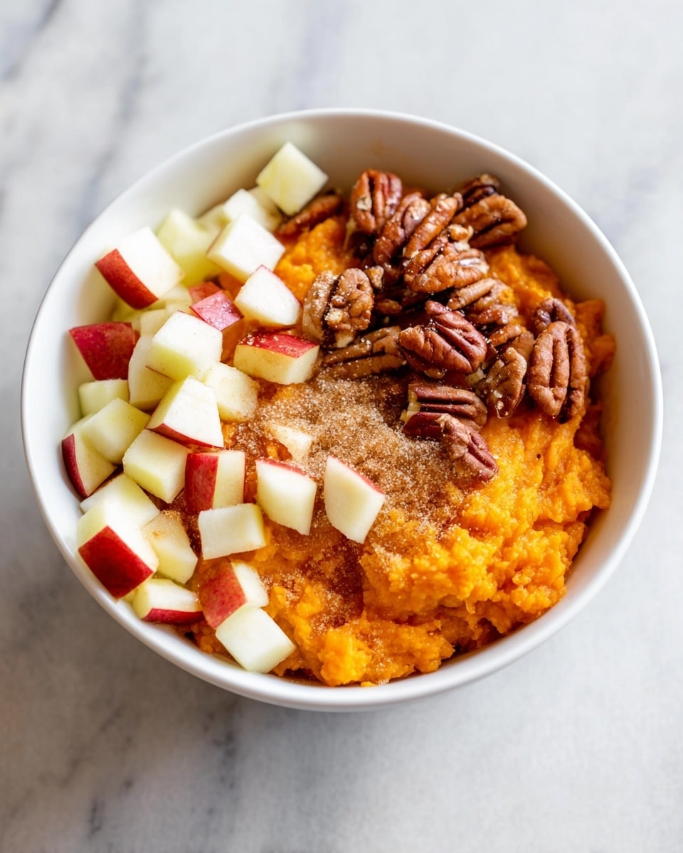A white bowl holds three distinct layers of food: at the bottom, there is a dense layer of bright orange mashed sweet potato with a soft, slightly chunky texture; on one side, a pile of small, diced apple pieces with red skin and white flesh adds a fresh, crisp contrast; on the other side, a cluster of glossy brown pecan halves provides a smooth, firm texture; a light sprinkle of brown sugar rests on top of the mashed sweet potato, adding a grainy and crystalline texture. The bowl is placed on a white marbled surface. photo taken with an iphone --ar 4:5 --v 7