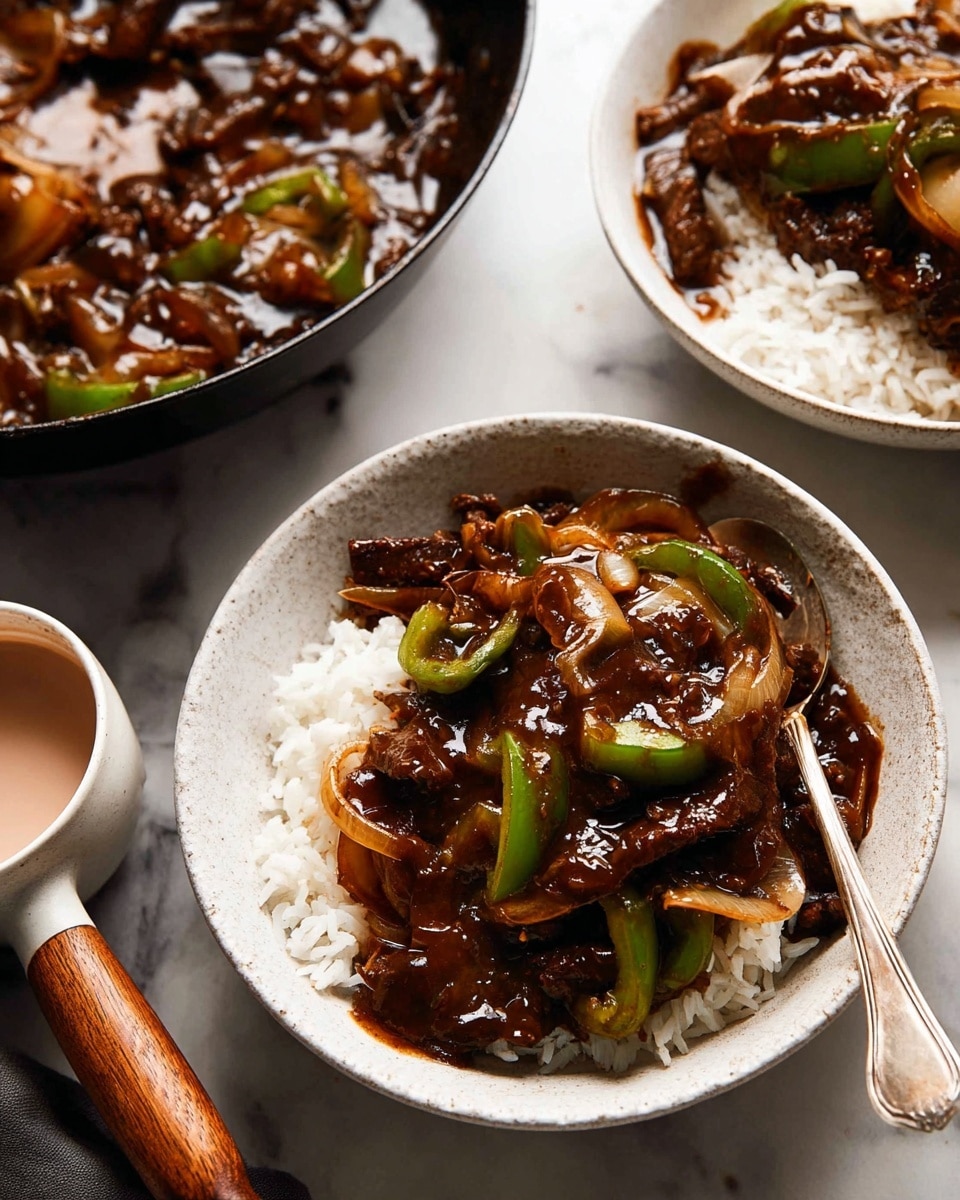 The image shows a bowl filled with a layer of white rice at the bottom and topped with a thick, glossy dark brown sauce mixed with pieces of green bell peppers, caramelized onions, and slices of beef. The bowl is white and textured with a spoon resting inside it. Nearby, there is another white bowl with more of the same dish and a small white cup filled with a pale pink liquid. The background surface is a white marbled texture, and part of a black pan with a wooden handle containing more of the dish is visible in the lower left corner. photo taken with an iphone --ar 4:5 --v 7