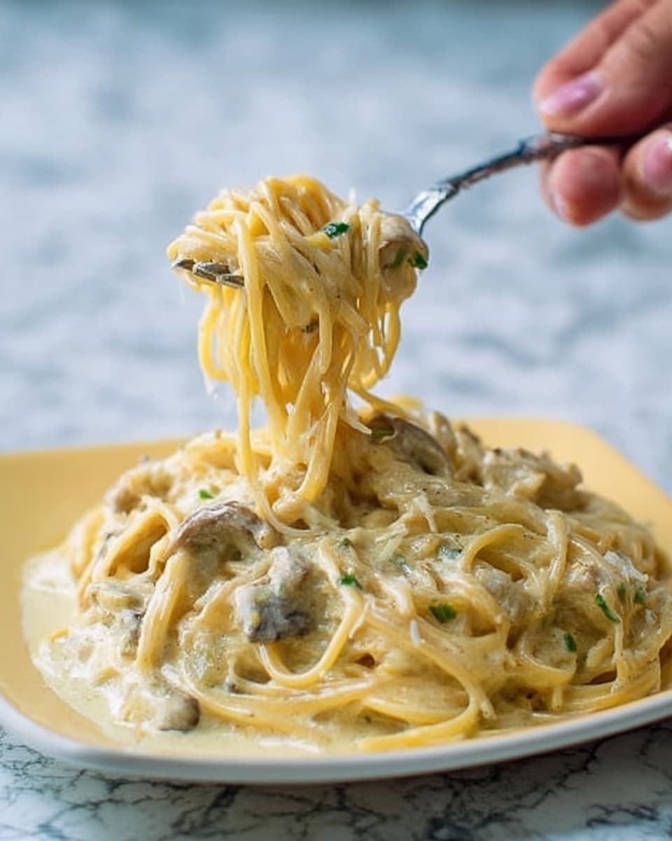 The image shows a close-up of creamy spaghetti pasta piled on a square white plate. The pasta is coated in a thick, pale yellow sauce with visible small bits of green herbs and mushrooms mixed in. A woman's hand is holding a fork, lifting a twirl of spaghetti off the plate, showing the smooth texture of the noodles and sauce. The background has a white marbled surface that contrasts with the creamy pasta. Photo taken with an iphone --ar 4:5 --v 7