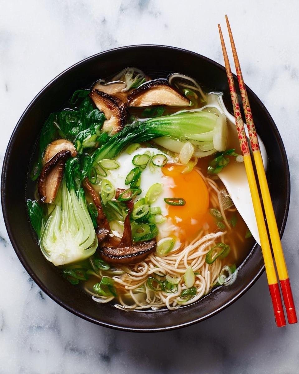 A black bowl filled with a noodle soup resting on a white marbled surface, containing a layer of thin, light beige noodles at the base, topped with bright green bok choy leaves and white stalks, several brown, grilled shiitake mushroom slices, and a soft poached egg with a runny orange yolk spreading over the noodles. The soup broth is clear and light brown, filling the bowl around the ingredients. Green sliced scallions are scattered on top for garnish. On the right side of the bowl rests a white soup spoon and a pair of yellow and red chopsticks. photo taken with an iphone --ar 4:5 --v 7