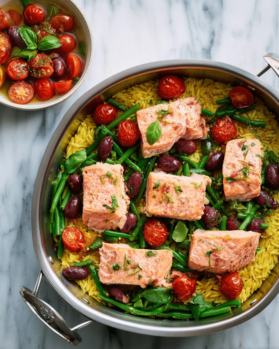 A metal pan filled with a base layer of yellow orzo pasta, topped with a green layer of cut green beans and scattered dark purple olives, and four pieces of light pink cooked salmon arranged evenly on top. Each salmon piece is garnished with bright red halved cherry tomatoes and small green basil leaves. On the left side next to the pan, there is a small white bowl with extra cherry tomatoes and basil leaves in a light dressing. The scene is set on a white marbled surface. Photo taken with an iphone --ar 4:5 --v 7