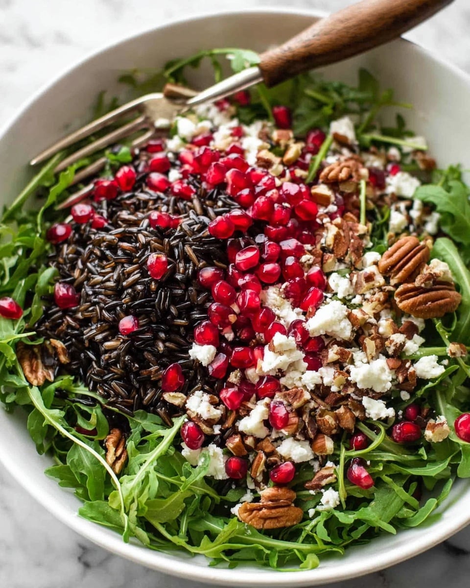 A white bowl on a white marbled surface holds a salad with six layers of ingredients arranged side by side. Starting from the left, there is a dark wild rice layer with a rough texture, next to bright green leafy greens, then white crumbled cheese scattered over the center, beside a section of brown pecans with a wrinkled texture, followed by dark dried berries, and finally a bright green layer of sliced scallions. Bright red pomegranate seeds fill the front part of the bowl, shining with moisture. Above the bowl, a clear glass container pours a thick, yellow dressing onto the cheese and greens. A blurred pomegranate half and scattered seeds appear in the background. Photo taken with an iphone --ar 4:5 --v 7