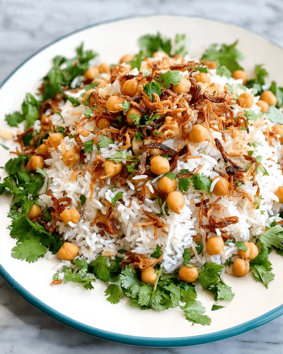 A white plate holds a mixed rice dish layered with fluffy white rice, golden chickpeas scattered throughout, and fresh green cilantro leaves spread on top and around. There are small pieces of crispy fried shallots or onions adding a crunchy texture and a light brown color contrast. The rice and chickpeas form the base layer with the herbs and fried shallots as the top layers, all set on a white marbled surface. photo taken with an iphone --ar 4:5 --v 7